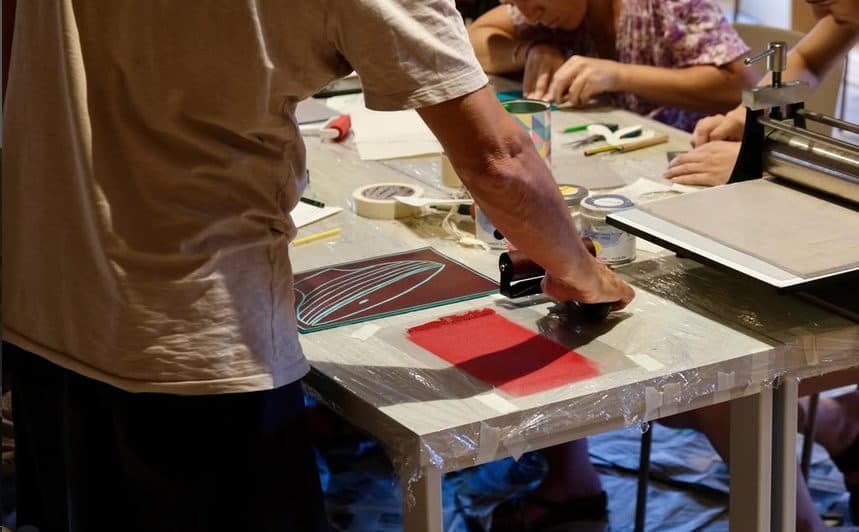 Participantes entintando una plancha con un rodillo en la mesa del taller